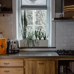 Przytulna kuchnia w stylu francuskiej wsi z ceglaną ścianą, drewnianymi frontami i roślinami przy oknie.