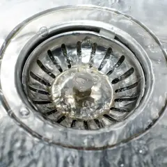 Woda stoi w zlewie, mimo że rury drożne a woda nie spływa. Widać metalowy syfon i strumienie wody.
