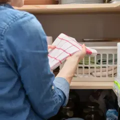 Kobieta układa ściereczki w koszyku, pokazując, gdzie wieszać ścierki w kuchni.