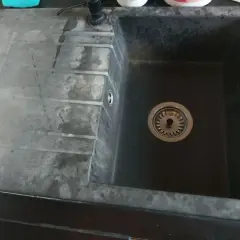Uszkodzony zlew granitowy z widocznymi zaciekami i osadem. Widać odpływ z sitkiem.