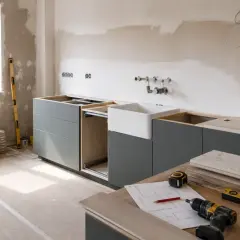 Trwa remont kuchni. Zamontowane szare szafki, biały zlew, widoczne narzędzia i plany.