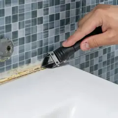 Narzędzie usuwa stary silikon z wanny. Przygotowanie do wymiany silikonu.