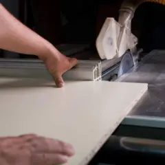 Ręce prowadzą płytę meblową do piły tarczowej, pokazując, jak wyciąć otwór w płycie meblowej.