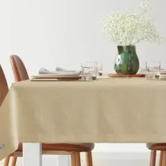 Elegancki obrus to świetny sposób, jak zabezpieczyć stół przed zarysowaniem. Na stole nakrycie, szklanki, talerze i wazon z kwiatami.