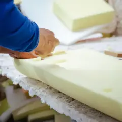 Ręce pracownika precyzyjnie tną gąbkę tapicerską, przygotowując ją do dalszej obróbki.