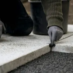 Ręce w rękawiczkach wykonują fugę na zewnątrz, układając kamienne płyty.
