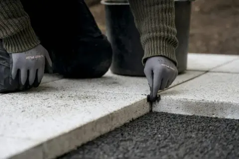 Ręce w rękawiczkach wykonują fugę na zewnątrz, układając kamienne płyty.