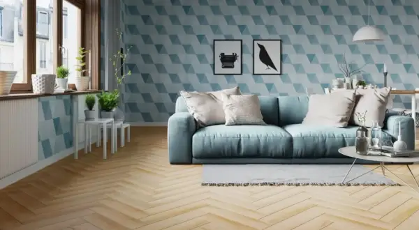 Jasny salon z błękitną kanapą i geometryczną tapetą. Podłoga z drewna ułożona w klasyczną jodełkę dodaje elegancji.