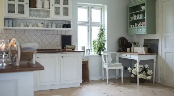 Biała kuchnia w stylu rustykalnym z widocznymi pilastrami meblowymi na szafkach i komodzie.