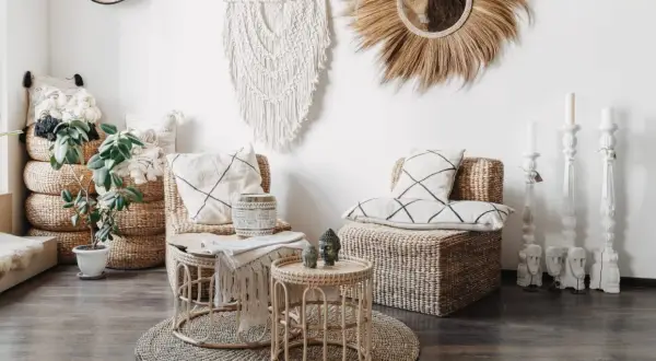 Przytulny salon w stylu boho z wiklinowymi meblami, makramą na ścianie i roślinami.
