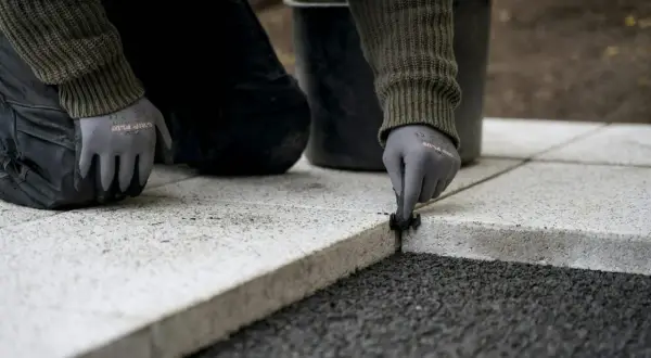 Ręce w rękawiczkach wykonują fugę na zewnątrz, układając kamienne płyty.