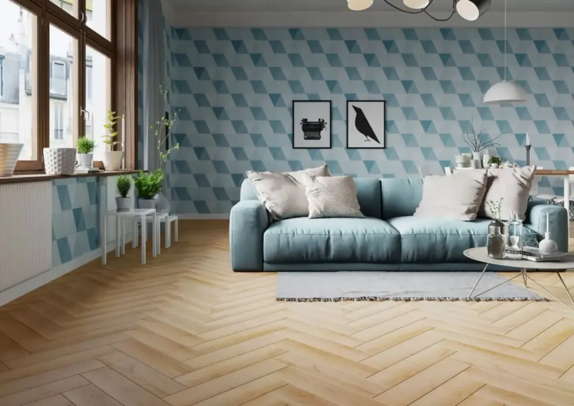 Jasny salon z błękitną kanapą i geometryczną tapetą. Podłoga z drewna ułożona w klasyczną jodełkę dodaje elegancji.