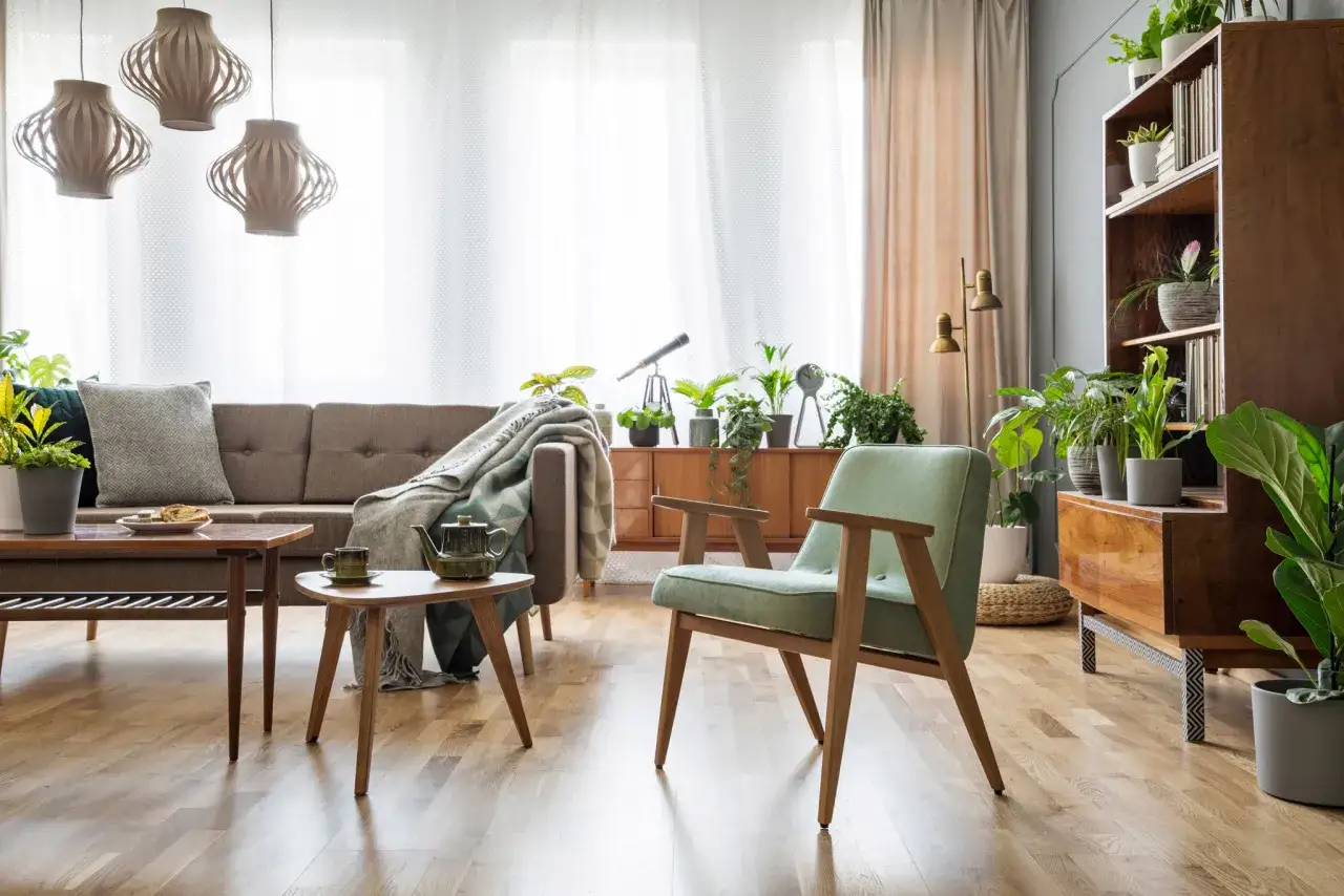 Przytulny salon z odnowionymi meblami PRL: kanapa, fotele, stoliki i regał pełen roślin.