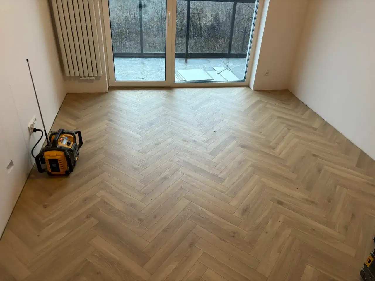 Nowe panele w jodełkę tworzą elegancką podłogę. W rogu stoi żółte urządzenie.