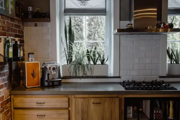 Przytulna kuchnia w stylu francuskiej wsi z ceglaną ścianą, drewnianymi frontami i roślinami przy oknie.